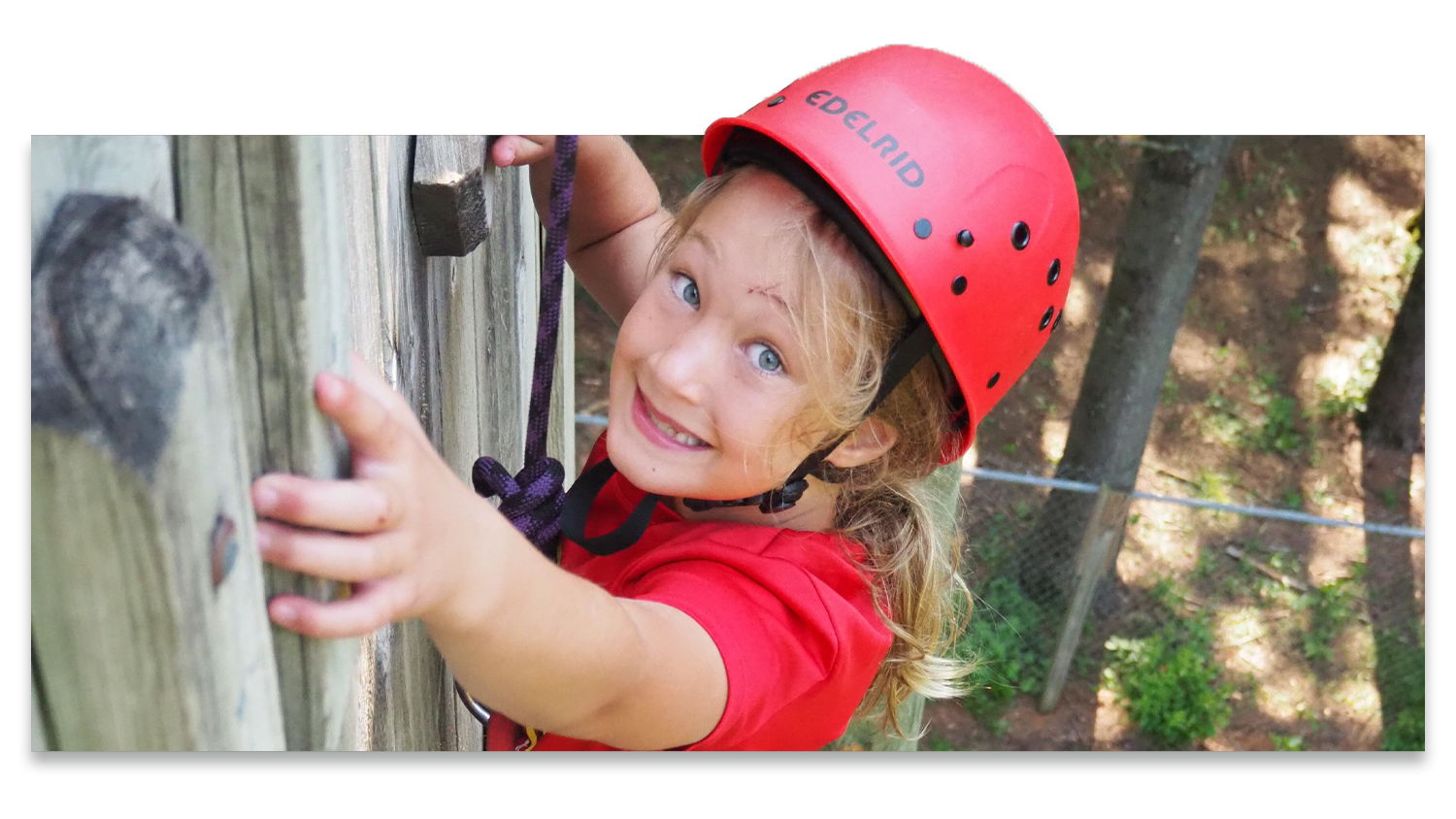 A young girl wearing climbing gear near the top of a 32-foot tall climbing wall