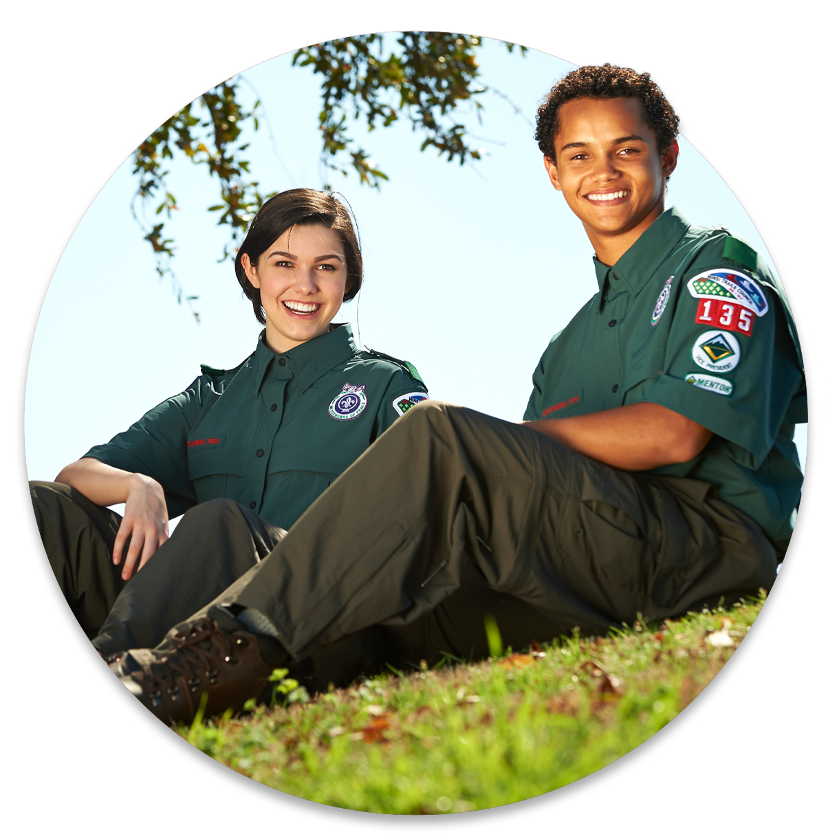 Two older teenagers smile while sitting outside wearing their venturing uniforms