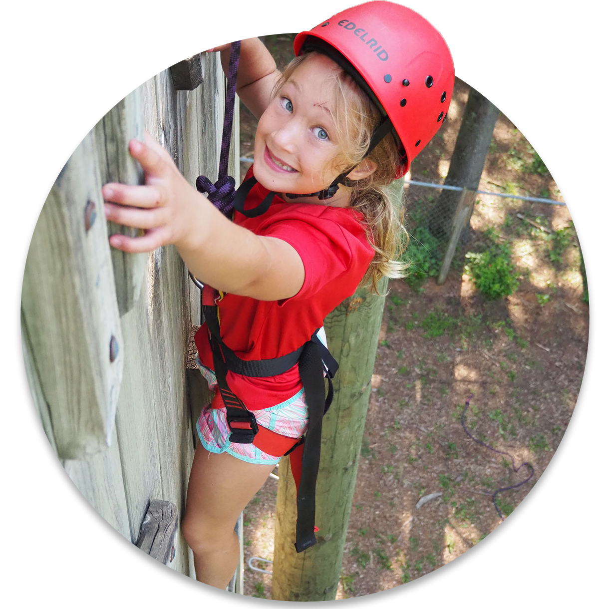 A young girl wearing climbing gear near the top of a 32-foot tall climbing wall